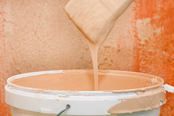 A can of paint and a brush against an old textured wall. Paint drips from the brush into the can. Room renovation concept