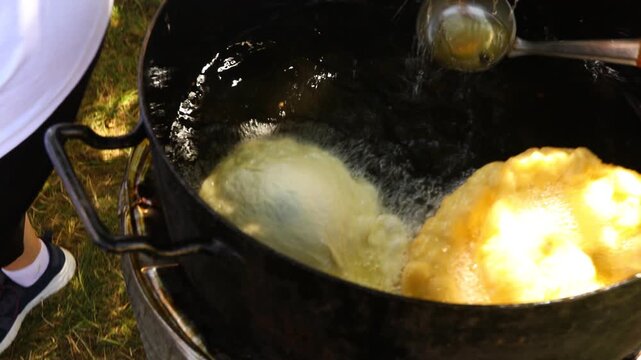 Traditionally way of cooking, frying dough in oil or pork fats making delicious treat in a large rustic pot, deep iron cauldron over open fire.