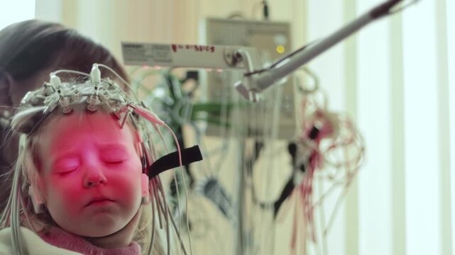 Child face, electroencephalography cap with electrodes. Closed eyes, expression of concentration or discomfort. Medical equipment records brain activity.