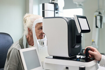 Senior Caucasian woman undergoing eye examination using advanced ophthalmology equipment, technician operating diagnostic machine in clinical setting, focusing on vision health