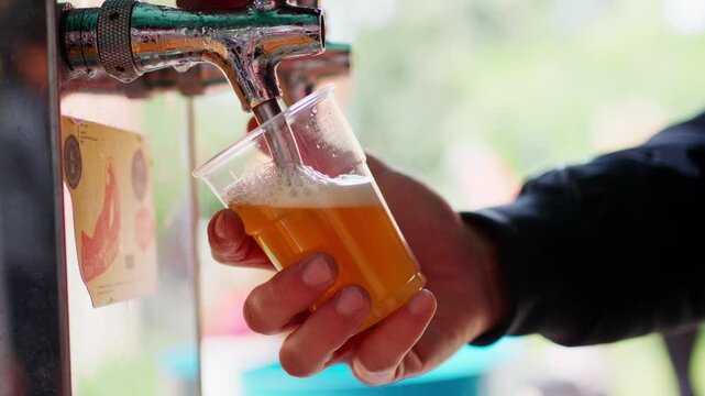 Person pouring draft beer into cup outdoors, relaxed, casual vibe