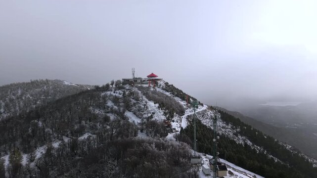 Snow covered Cerro Otto ridge with red-roof summit building and antennas during blowing winter snowstorm.