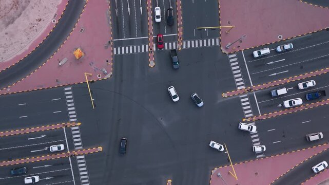Overhead drone view of a multi-lane intersection in Kuwait City with moving cars, crosswalks, signage, and desert edge&mdash;clean geometric layout for transport or smart-city themes.
