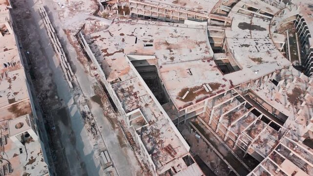 Oblique overhead drone of a semi-circular abandoned construction site with exposed beams, cracked slabs, stains and debris&mdash;gritty demolition survey urbex visual no people.