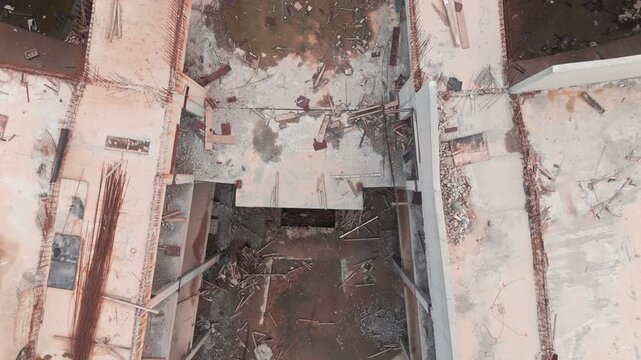 Aerial drone view of a massive, unfinished commercial building complex. Decaying concrete skeleton with unused materials and weeds, symbolizing economic recession and halted development.