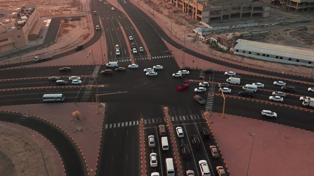 Golden-hour drone view of a signalized multi-lane intersection with busy vehicles, crosswalks, desert edge, and new developments&mdash;clean transport infrastructure plate, editorial or smart-city themes.