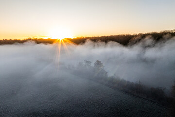 Aerial view of golden sunrise illuminating misty fields and silhouetting the treeline, Thames Valley, Oxfordshire, United Kingdom.
