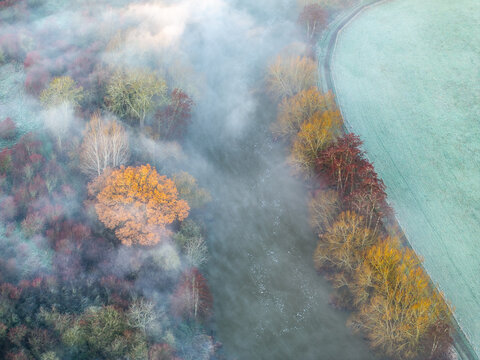 Aerial view of a serene countryside blanketed in mist, where autumnal hues meet the frosty fields, Thames Valley, Oxfordshire, United Kingdom.