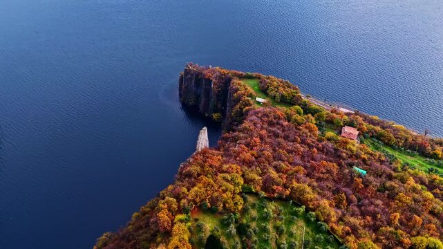 Aerial view of a rocky peninsula on Lago d&rsquo;Iseo surrounded by deep blue water and autumn forests, showing terraced fields and rural buildings in northern Italy.