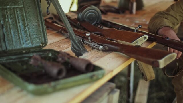 Close-up view of Red Army weapons display for Great Patriotic War reenactment. Mosin rifle, PPSH-41 drum magazine, and ordnance on wooden table