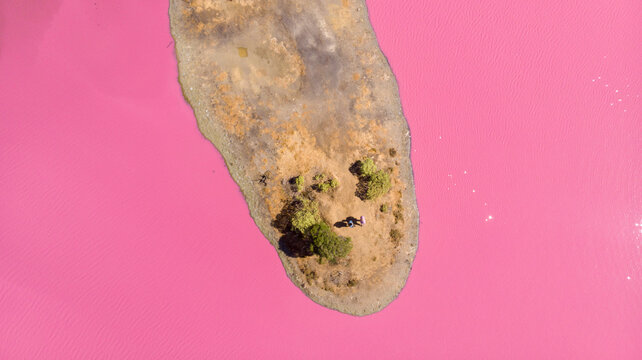 Aerial view of a striking pink lake contrasting with the earth-toned island, creating a surreal landscape of vibrant colors, Port Melbourne, Victoria, Australia.
