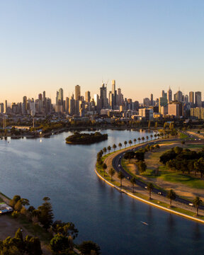 Aerial view of Albert Park Lake's tranquil waters reflecting the city skyline under a soft, golden light, Albert Park, Victoria, Australia.