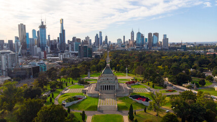 Aerial view of the Shrine of Remembrance standing proudly amidst verdant parklands, contrasting with the towering skyline beyond, Melbourne, Victoria, Australia.