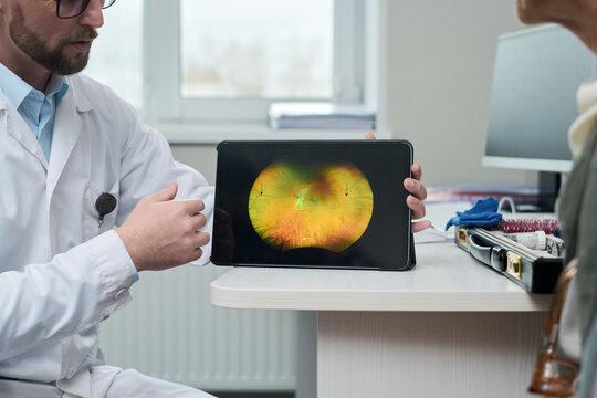 Caucasian middle aged male doctor showing digital retinal scan on tablet to senior Caucasian woman during medical consultation, discussing eye health and diagnostic results in clinic