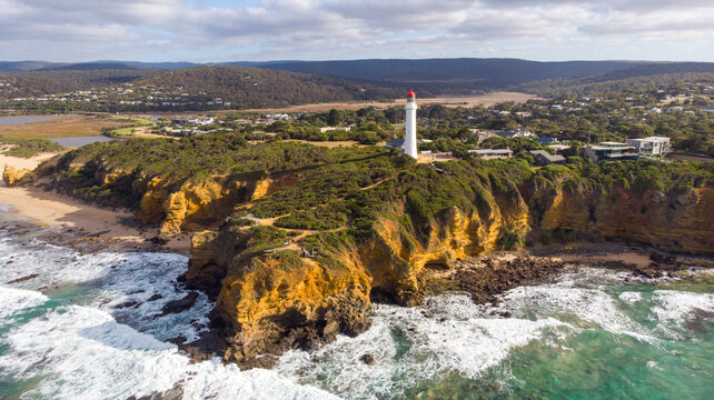Aerial view of the Split Point Lighthouse standing tall against the rugged coastline as waves crash against the cliffs, Split Point Lighthouse, Victoria, Australia.