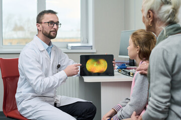 Caucasian male doctor showing retinal scan on digital tablet to senior Caucasian woman and...