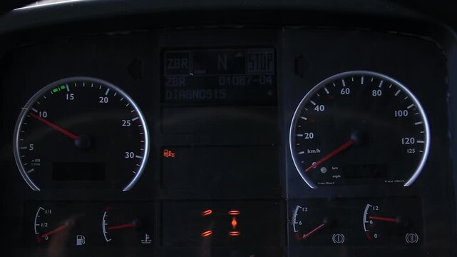 Close up view of a truck dashboard with illuminated gauges and warning lights. Digital screen displays neutral gear stop message and diagnosis text. Fuel and temperature gauges indicate low levels.