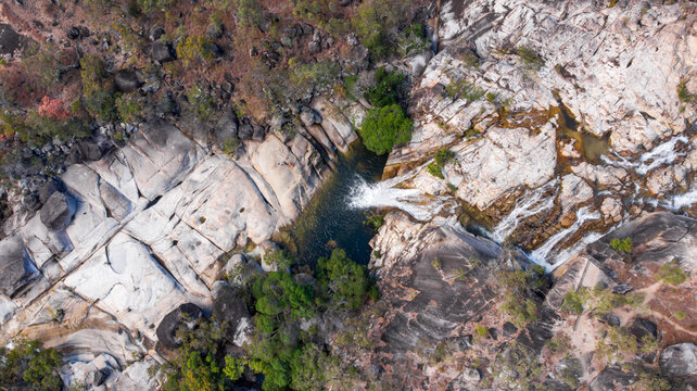 Aerial view of water cascading down rugged rock formations, carving a path through the landscape at Emerald Falls, Queensland, Australia.