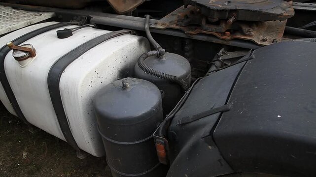 Close up of truck underside revealing fuel system and air brake components. White plastic fuel tank and steel air reservoirs are secured to metal chassis. Visible are connecting hoses