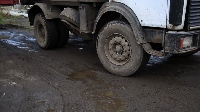 Heavy duty dump truck navigating muddy unpaved road. Wheels caked with thick, dark brown mud, water splashes. Captures challenging terrain, power.