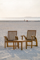 Relaxing image of two wooden Chairs at the beach with a white sandy beach in the background. 