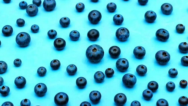 Numerous fresh blueberries scattered artfully across a vibrant cyan blue background creating a healthy fruit pattern backdrop