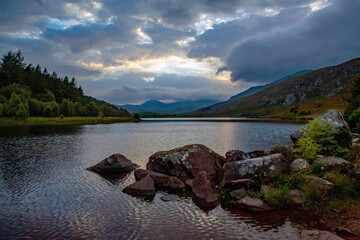 The calm before the storm. Storm clouds hiding a sunset reflected with the mountains into the still water of a mountain lake, Llyn Mymbyr, Snowdonia, Wales