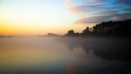 Misty morning sunrise colours reflected in a still lake. Swithland Reservoir, Leicestershire