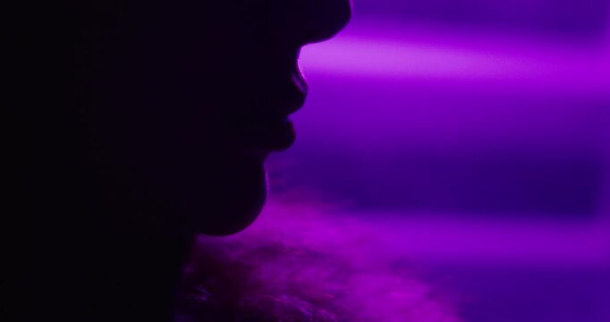 Artistic close-up of a woman&rsquo;s mouth and lower face silhouetted against glowing purple neon fog, creating a moody and cinematic visual atmosphere.