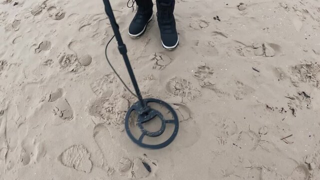 Metal detector sweeping over disturbed beach sand and footprints as a person searches for lost metallic items.