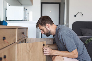 Man opening drawer at home, focused and thoughtful in modern apartment interior, real people lifestyle, authentic everyday domestic routine, casual living moment