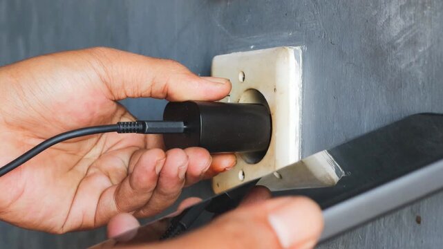 Man's hand view plugging a mobile phone charger cable into a wall socket. Ready to connect, plug in electricity