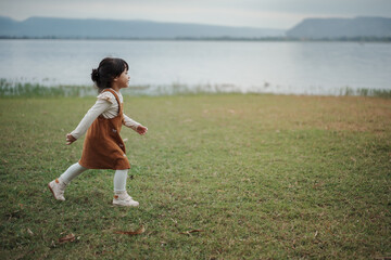 happy toddle girl walking on grass field near the river