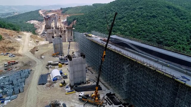 Drone view of a large viaduct deck under construction with extensive scaffolding and formwork at a highway construction site. Civil engineering and infrastructure development in mountainous terrain.