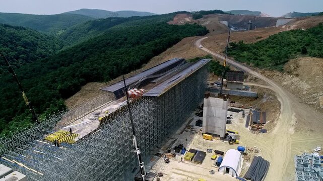 Drone view of a large viaduct deck under construction with extensive scaffolding and formwork at a highway construction site. Civil engineering and infrastructure development in mountainous terrain.
