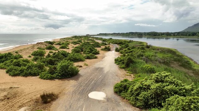 Aerial view of a sandy path lined with green bushes, separating the calm sea from the tranquil lake in a scenic landscape, Korission, Corfu, Greece.