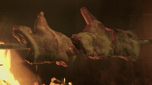 half-roasted suckling pigs on a spit with a wood fire in the background