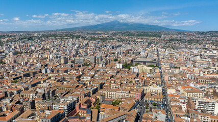 Obraz premium Aerial view of the city center of Catania, Sicily, southern Italy. In the background, on the horizon, Mount Etna looms in silhouette, dominating the panorama. It is a sunny summer day.