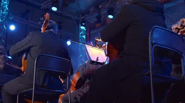 Music Under Lights, Intimate Shot Capturing String Section Under Blue Lighting With Conductor In Background. Media