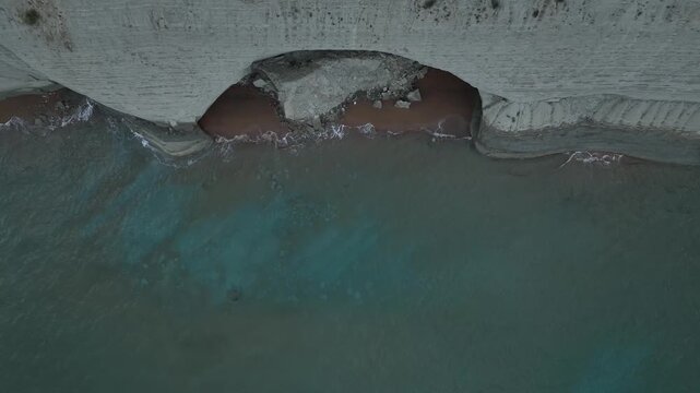 Aerial view of the stark contrast between the pale cliffs and the deep turquoise ocean waters meeting the sandy shore, Agios Stefanos, Greece.