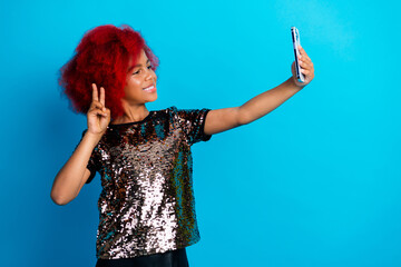 Young stylish girl takes selfie with peace sign against blue background