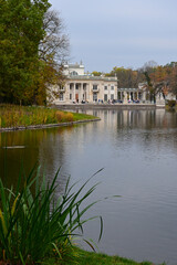 Fototapeta premium Autumn time in Warsaw's Royal Baths Park (in Polish: Lazienki Krolewskie). Palace on the Water and pond with reflections in the water. Warsaw, Poland 