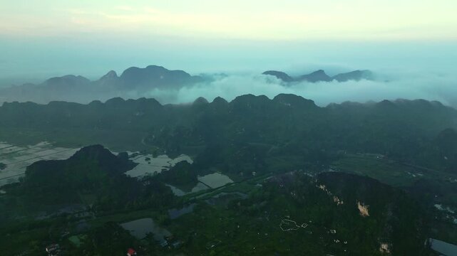 Aerial view of rugged, verdant mountains shrouded in ethereal mist, creating a serene landscape, Hoa Lu, Ninh Binh, Vietnam.
