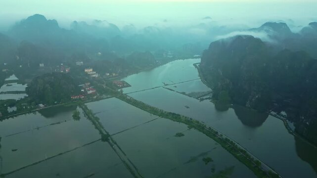 Aerial view of Tam Coc's flooded rice paddies reflecting the surrounding limestone karst mountains under a blanket of mist, Hoa Lu, Ninh Binh, Vietnam.