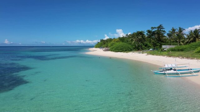 Aerial view of boats resting on the white sandy beach, bordering turquoise waters and vibrant green trees, Carles, Western Visayas, Philippines.