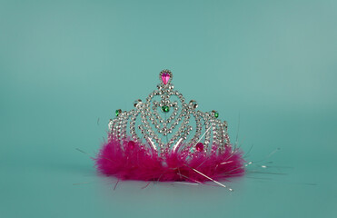 Children's tiara with rhinestones and pink down on a blue background, center of frame, close-up. A toy accessory for a costume and a holiday. © nina blez