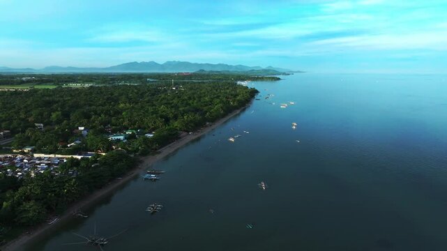 Aerial view of a coastal area, showing the contrast between the lush green vegetation and the dark blue of the water, Carles, Western Visayas, Philippines.