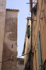 Two simple, square windows with white frames set into a weathered, rustic stone and plaster wall of an old European building under a terracotta roof. © Impresyjna