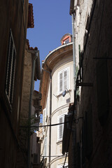 Two simple, square windows with white frames set into a weathered, rustic stone and plaster wall of an old European building under a terracotta roof. © Impresyjna