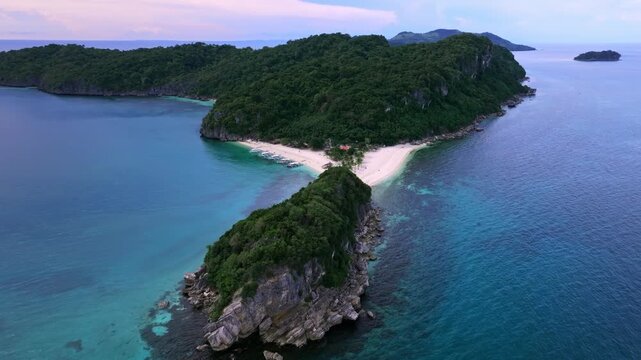 Aerial view of verdant green islands, white sands, and turquoise waters, where boats rest on the shore, Carles, Western Visayas, Philippines.